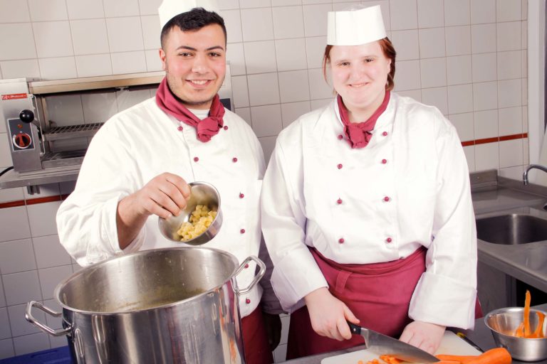 zwei Köche-Azubis aus dem Berufsbildungswerk Südhessen stehen gemeinsam am Kochtopf in der Ausbildungsküche