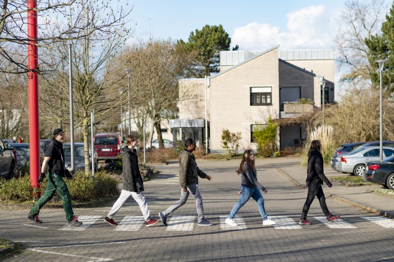 Gruppe Jugendliche marschiert wie die Beatles über die Abbey Road hintereinander über Zebrastreifen in das Berufsbildungswerk
