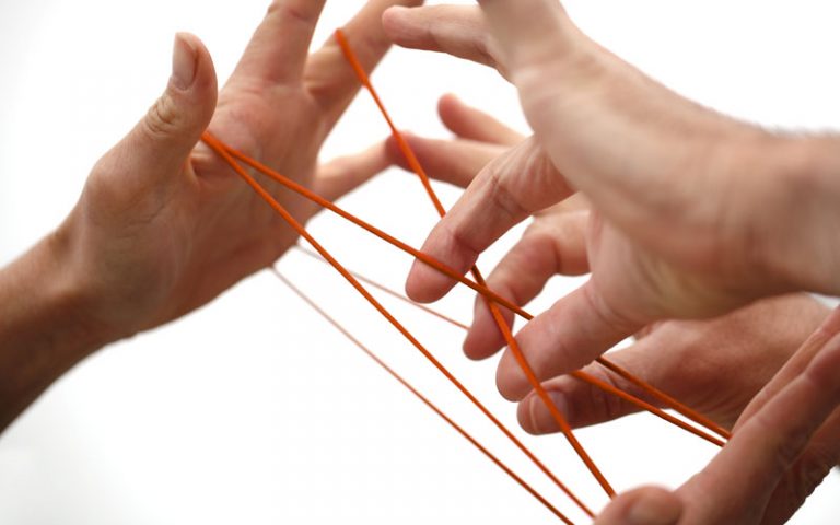 Vier Hände spielen mit einem orangenen Faden - bbw Südhessen - Netzwerk