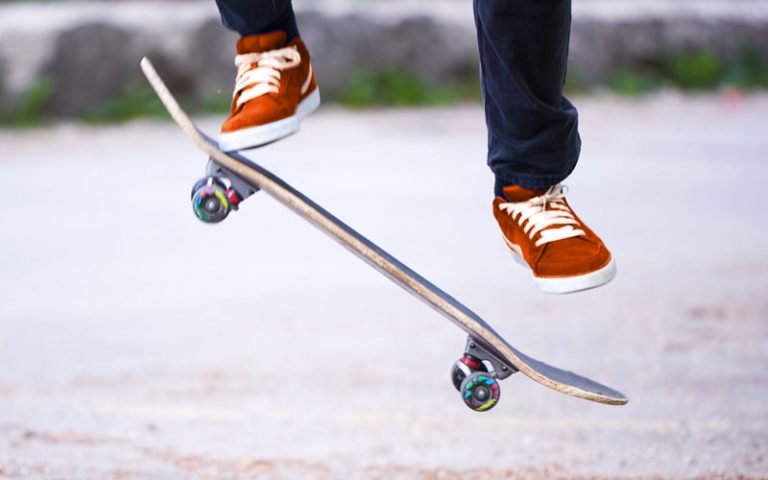 Beine mit orangenen Turnschuhen, darunter ein Skateboard. Der Skateboardfahrer macht gerade einen Sprung