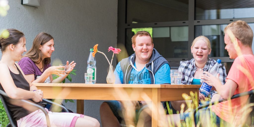 Gruppe Jugendliche des bbw Südhessen sitzen am Tisch auf der Terrasse und genießen die Freizeit