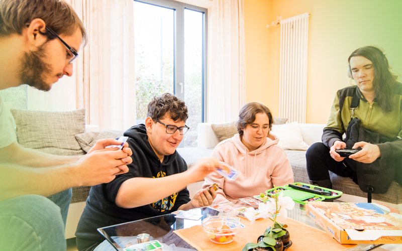 Gruppe Jugendlicher sitzen im Wohnzimmer am Tisch und spielen - Jugendhilfe bbw Südhessen