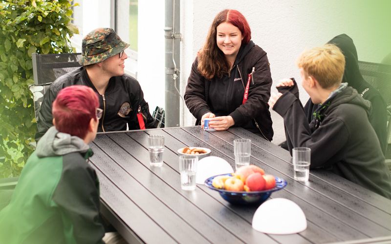 Gruppe Jugendliche sitzt am Tisch auf der Terrasse und führen Gespräche - Jugendhilfe bbw Südhessen - Wohnkonzepte